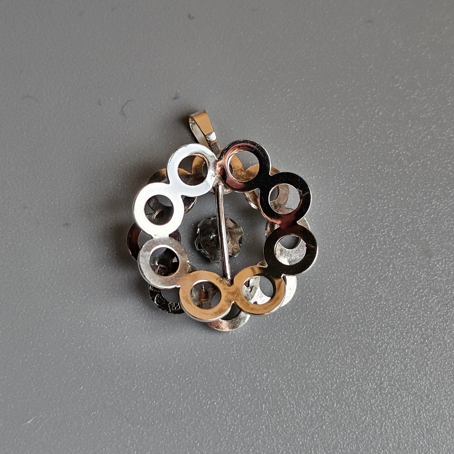 Circular pendant made of interconnected metallic rings in various colors.