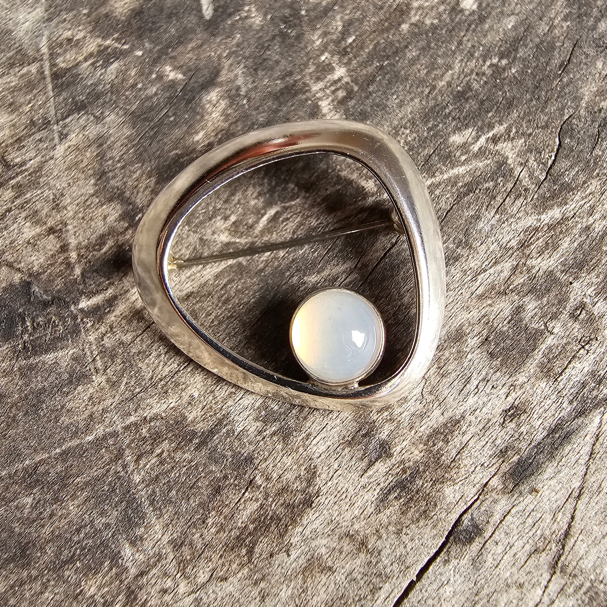 Silver ring with a round white pearl or moonstone set in an asymmetrical teardrop-shaped bezel.