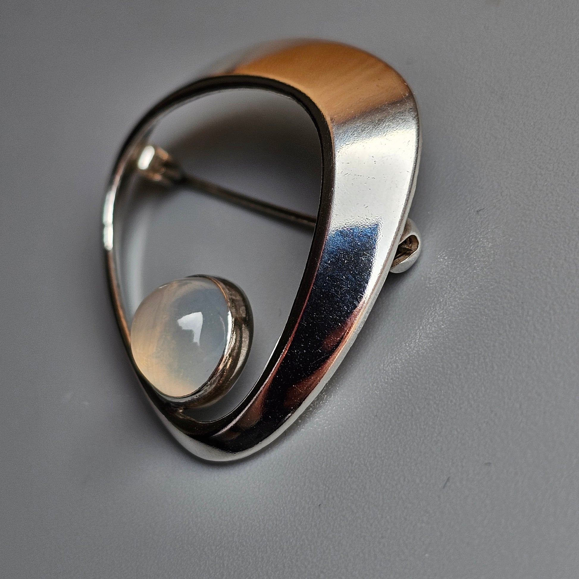 Sleek, modernist silver brooch with a curved teardrop shape and inset pearl.