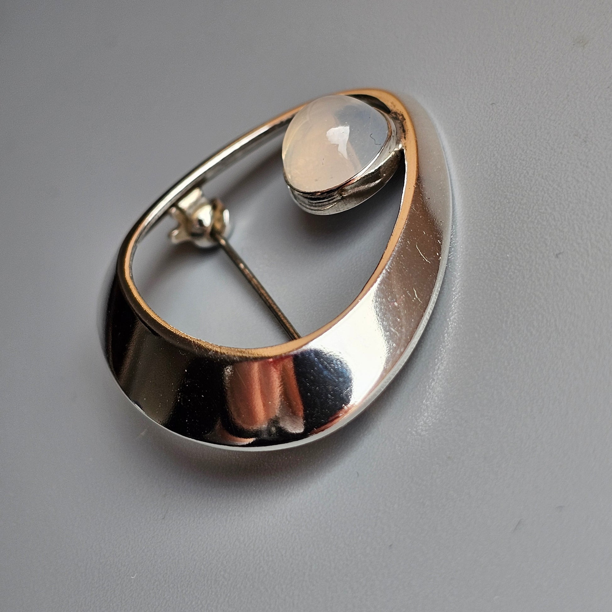 Teardrop-shaped silver brooch with a round gemstone accent.