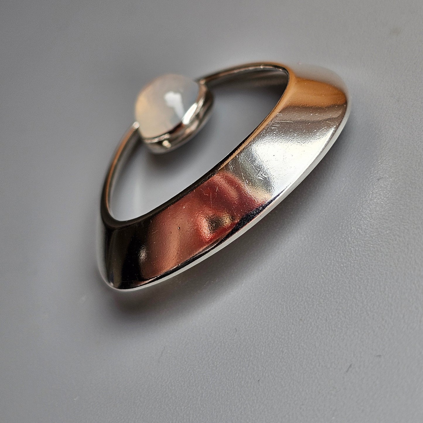 Sleek, modern silver ring with a curved, asymmetrical design and a small pearl-like accent.