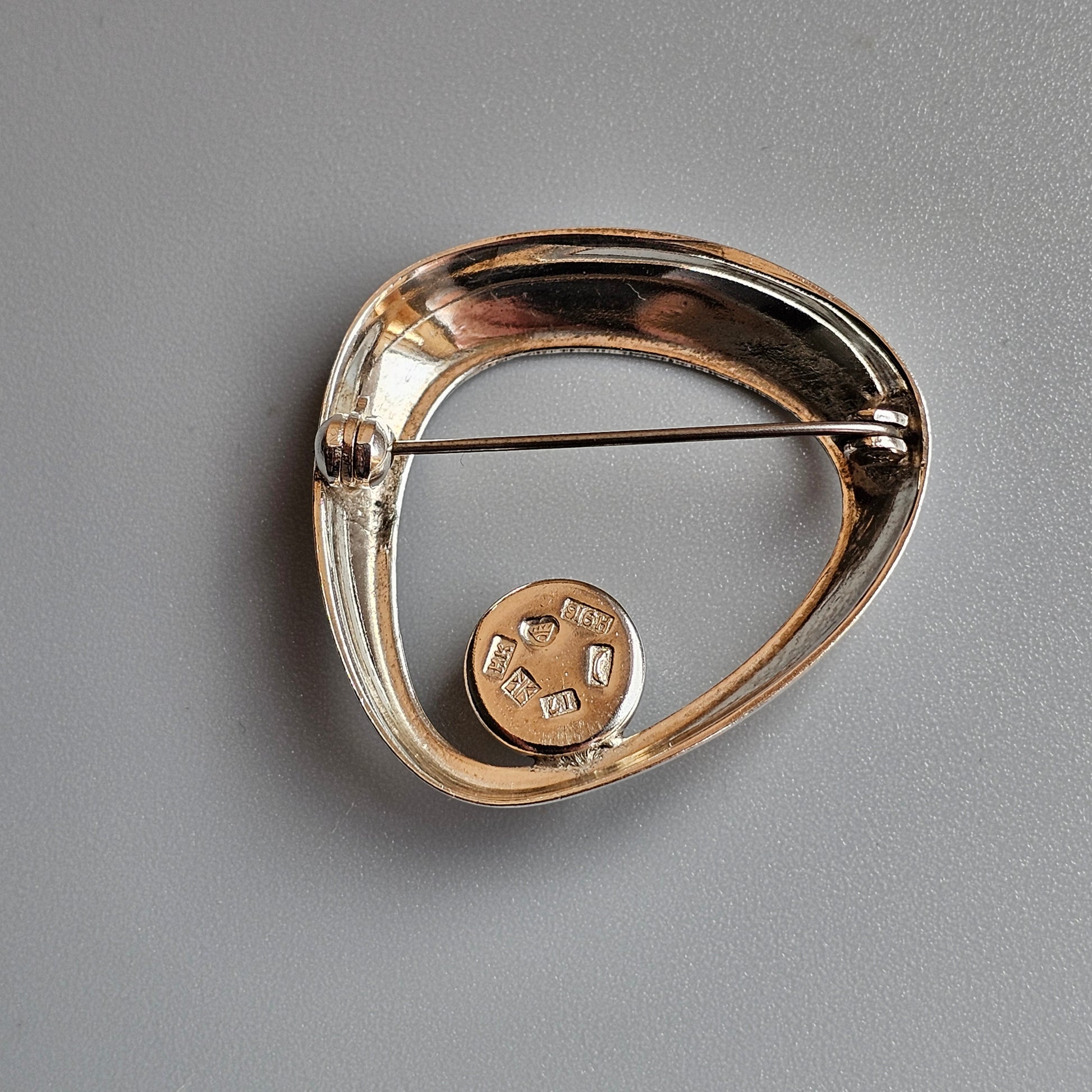 Gold-toned modernist brooch with an asymmetrical teardrop shape and circular accent.