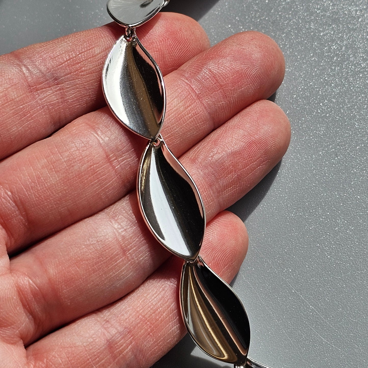 Silver pendant necklace with three leaf-shaped links held in a hand.