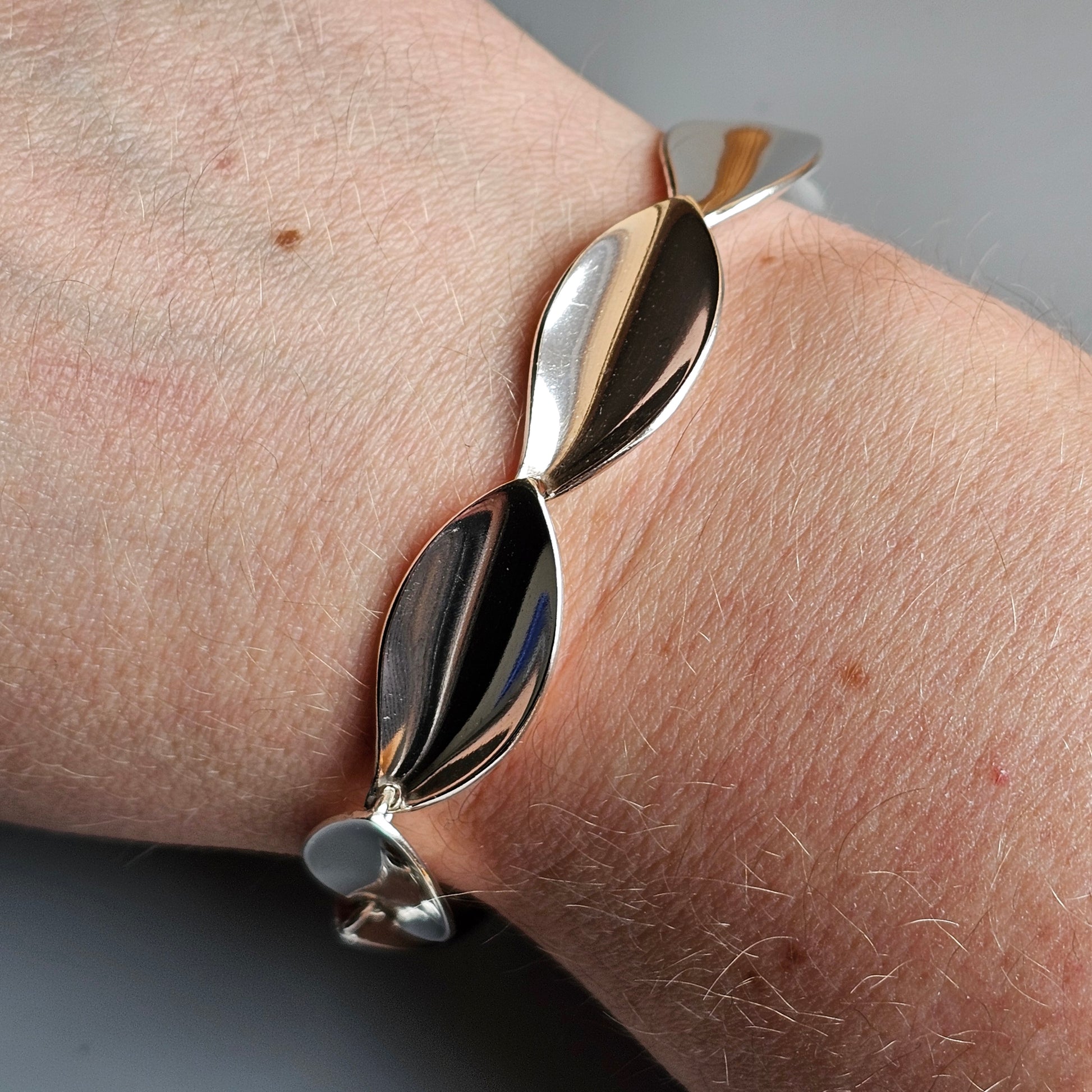 Silver bracelet with leaf-shaped links worn on a wrist.