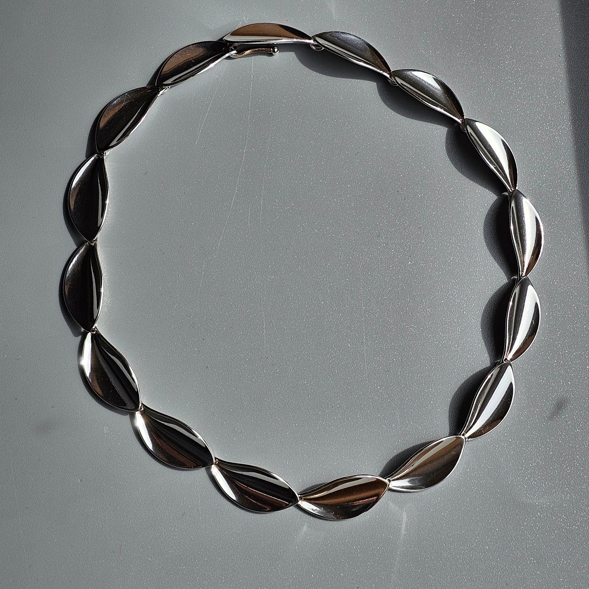 Circular necklace made of smooth, teardrop-shaped metallic beads.