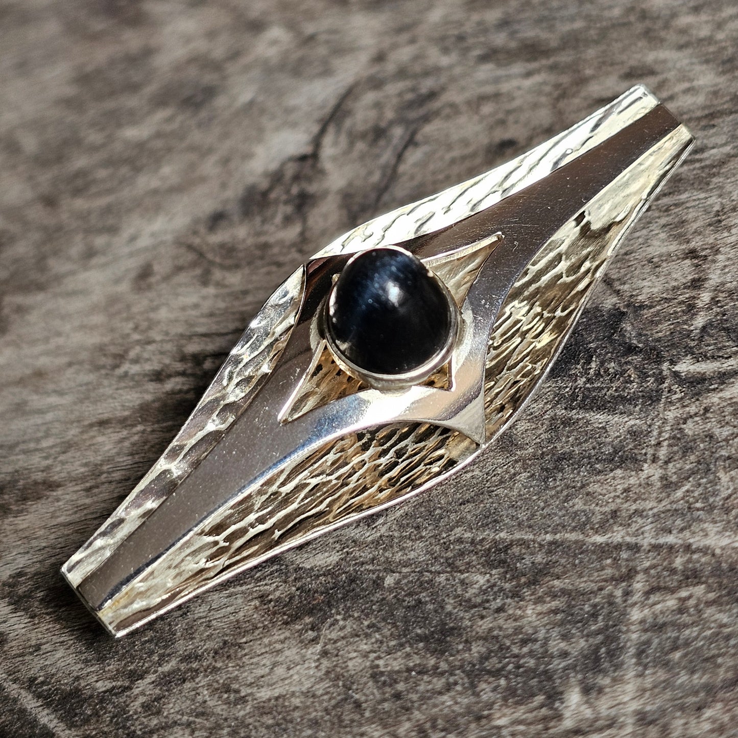 Silver ring with a black gemstone set in an elongated, textured design.