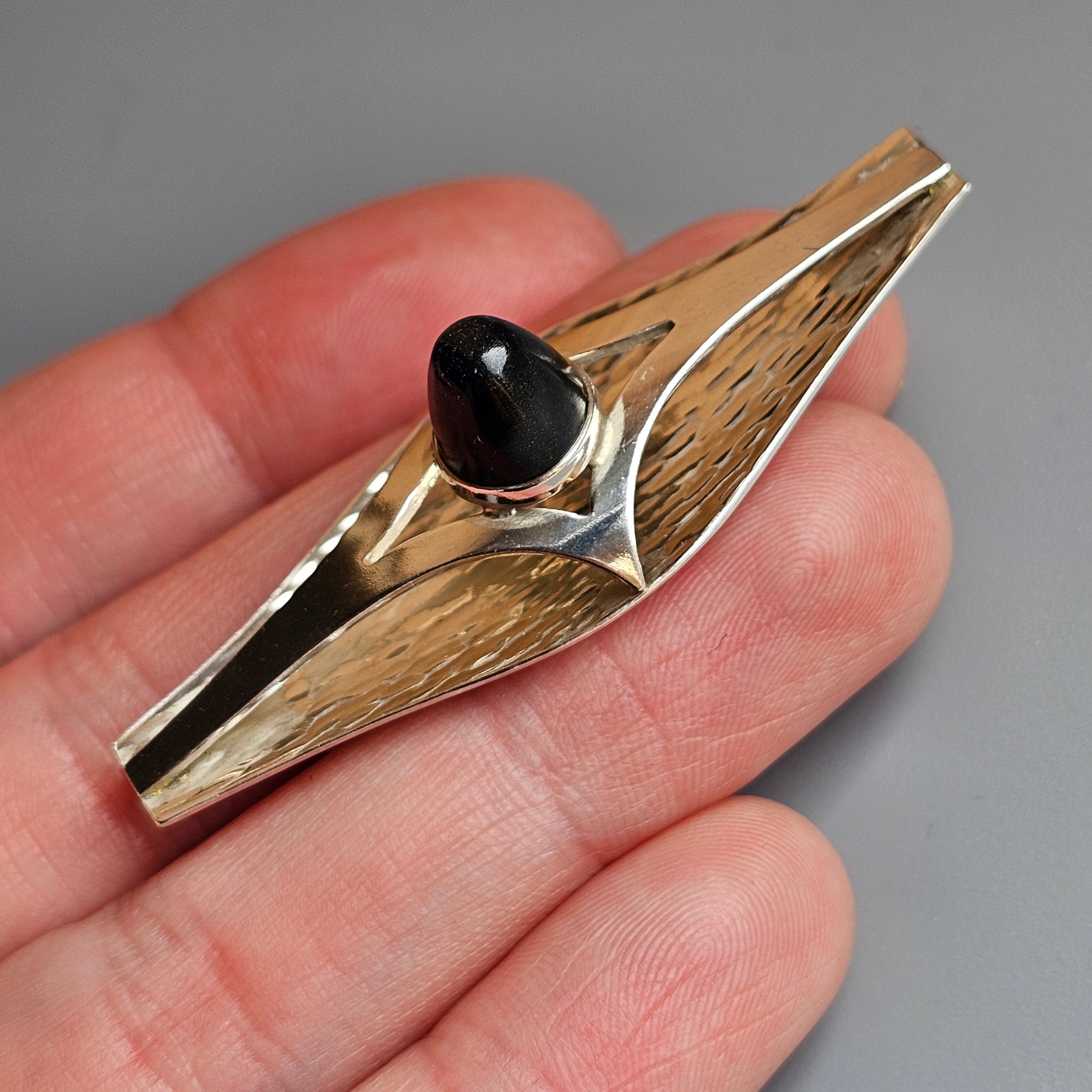 Wooden and metal kazoo with a black bead-like element held in a person’s hand.