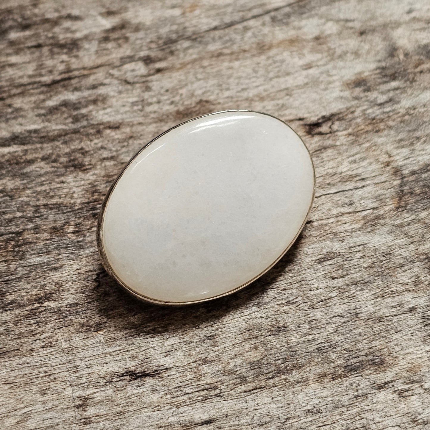 Oval-shaped white gemstone or cabochon with a metallic rim.