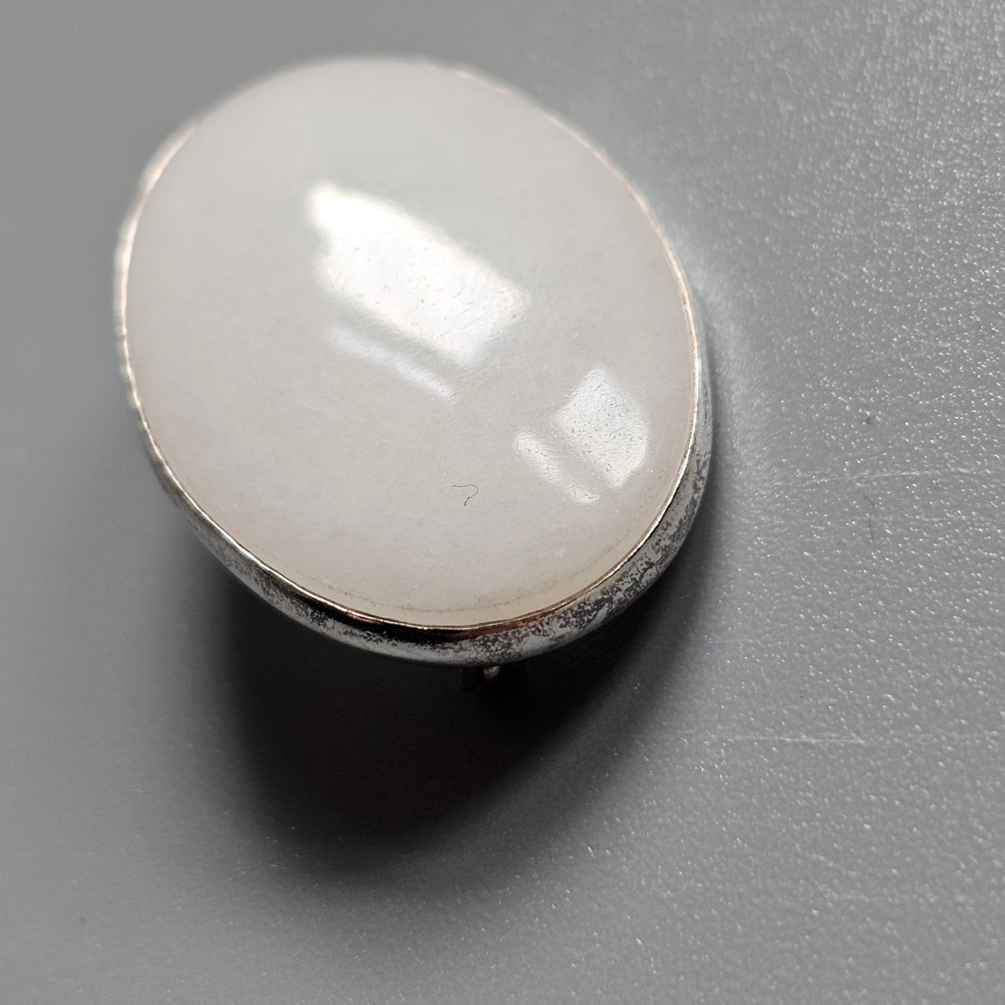 Oval-shaped white gemstone or cabochon set in a metal bezel.