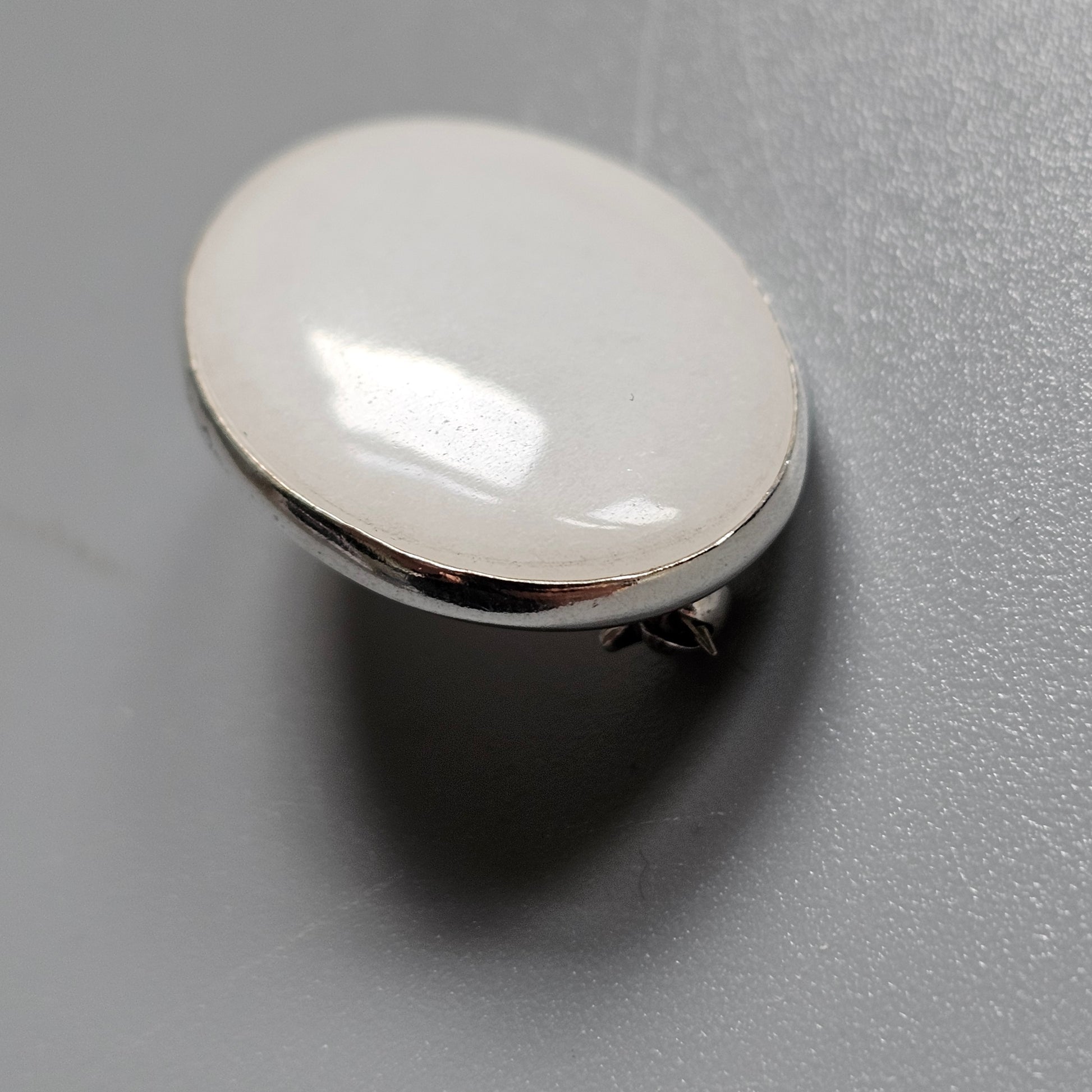 Oval-shaped, pearlescent button or decorative element with a metallic rim.