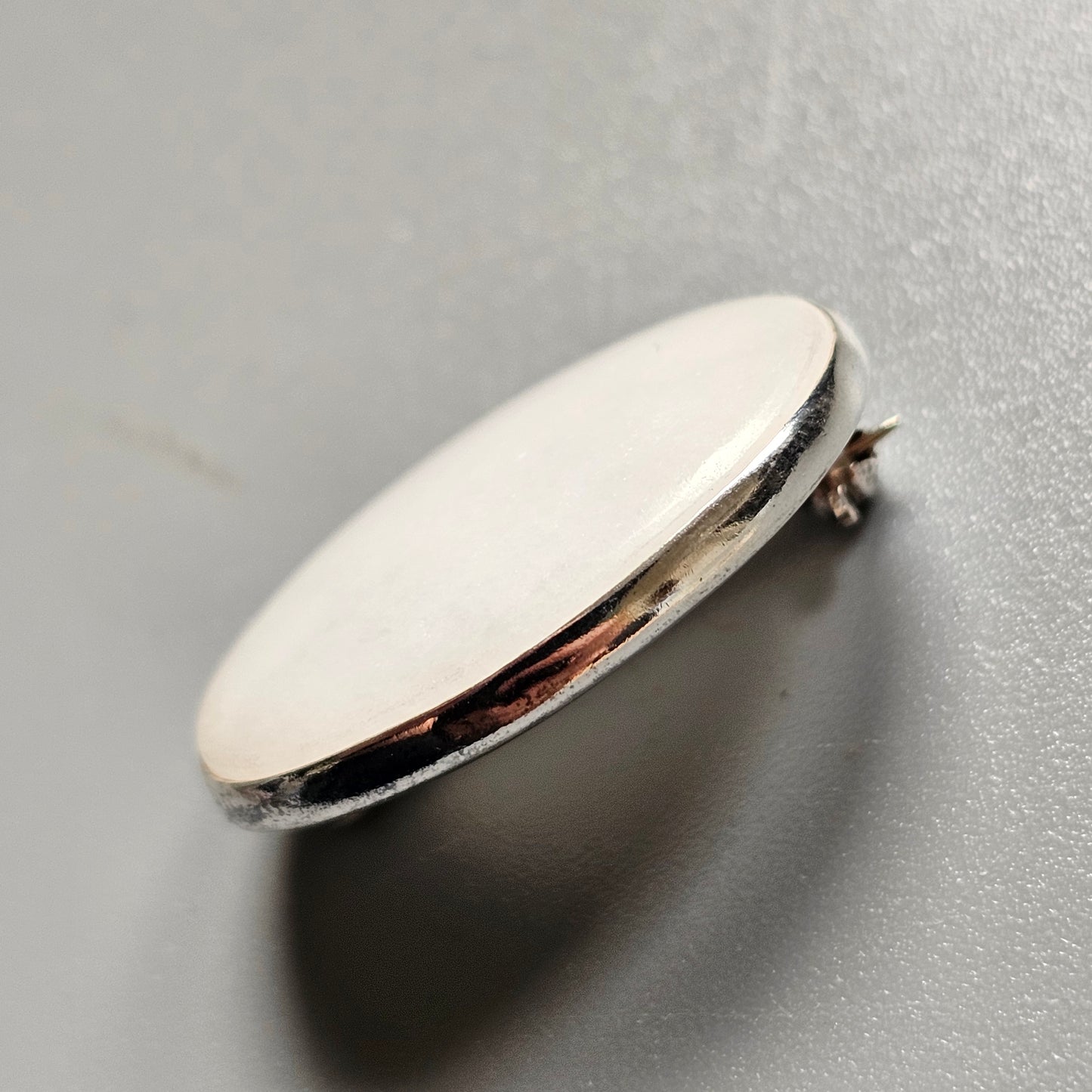 Oval-shaped silver metal button or pin with a flat surface.