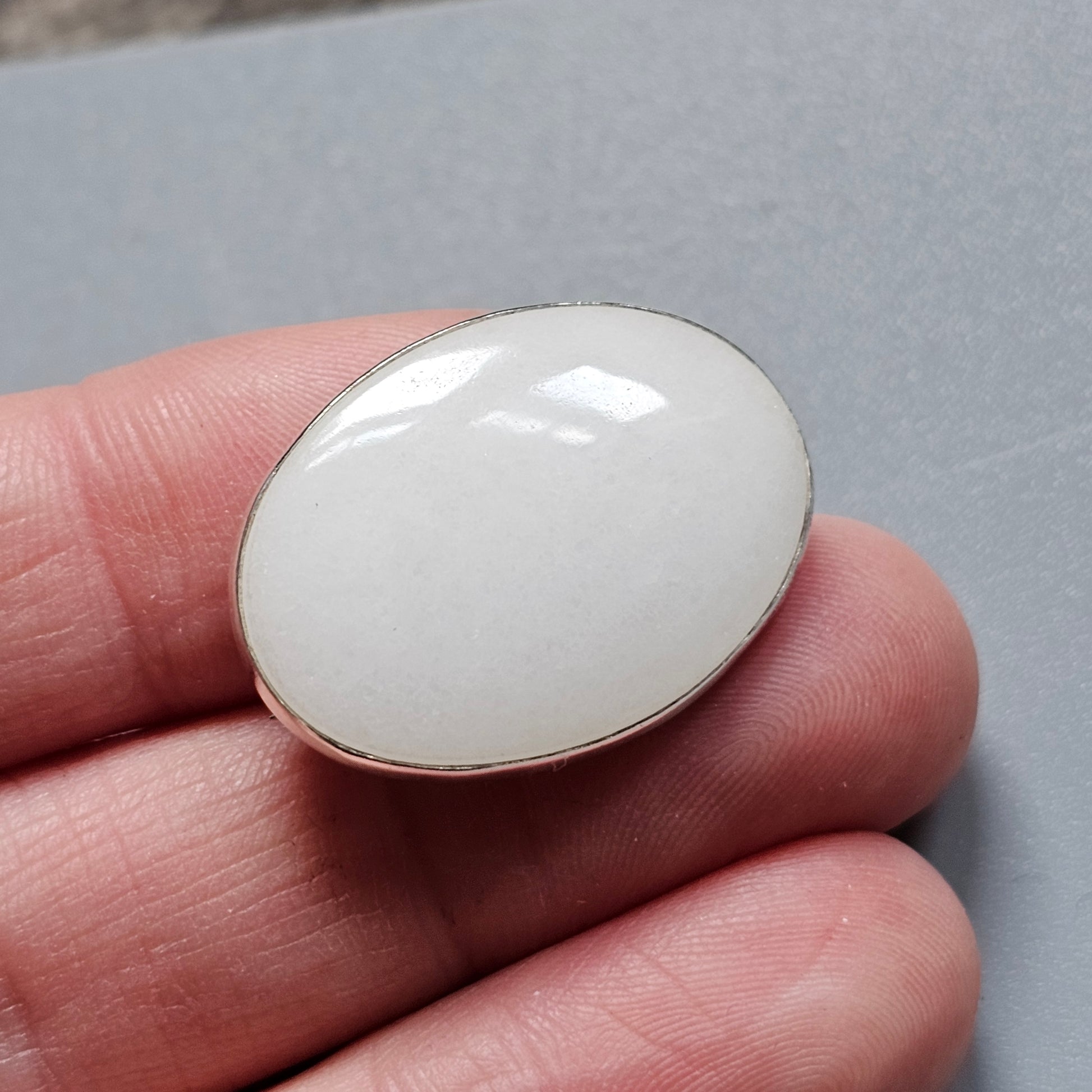 Oval-shaped white gemstone or cabochon held between fingers.