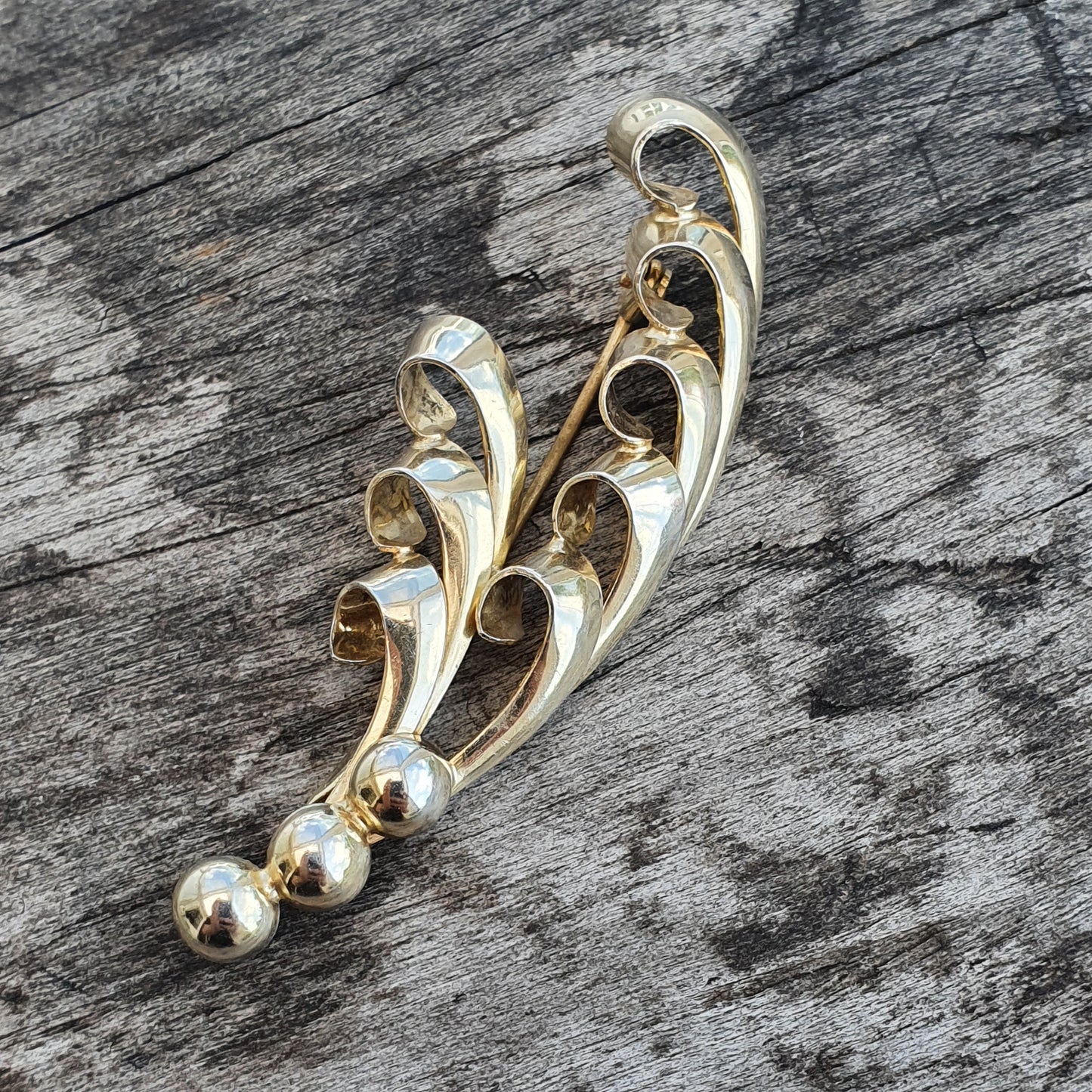 Gold-toned brooch with a swirling, abstract design and spherical ends.