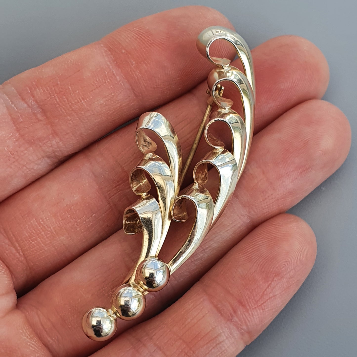 Elegant silver brooch with curved, flowing designs and small spherical ends.