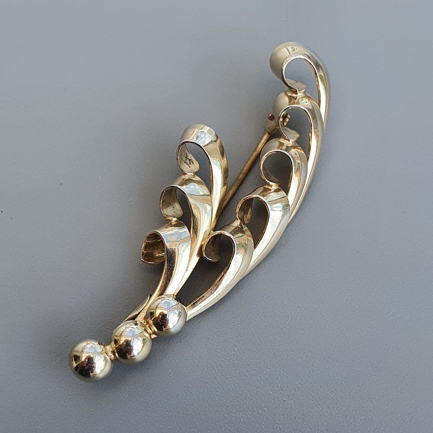 Gold-toned brooch with a curved, leaf-like design featuring small spheres at the ends.