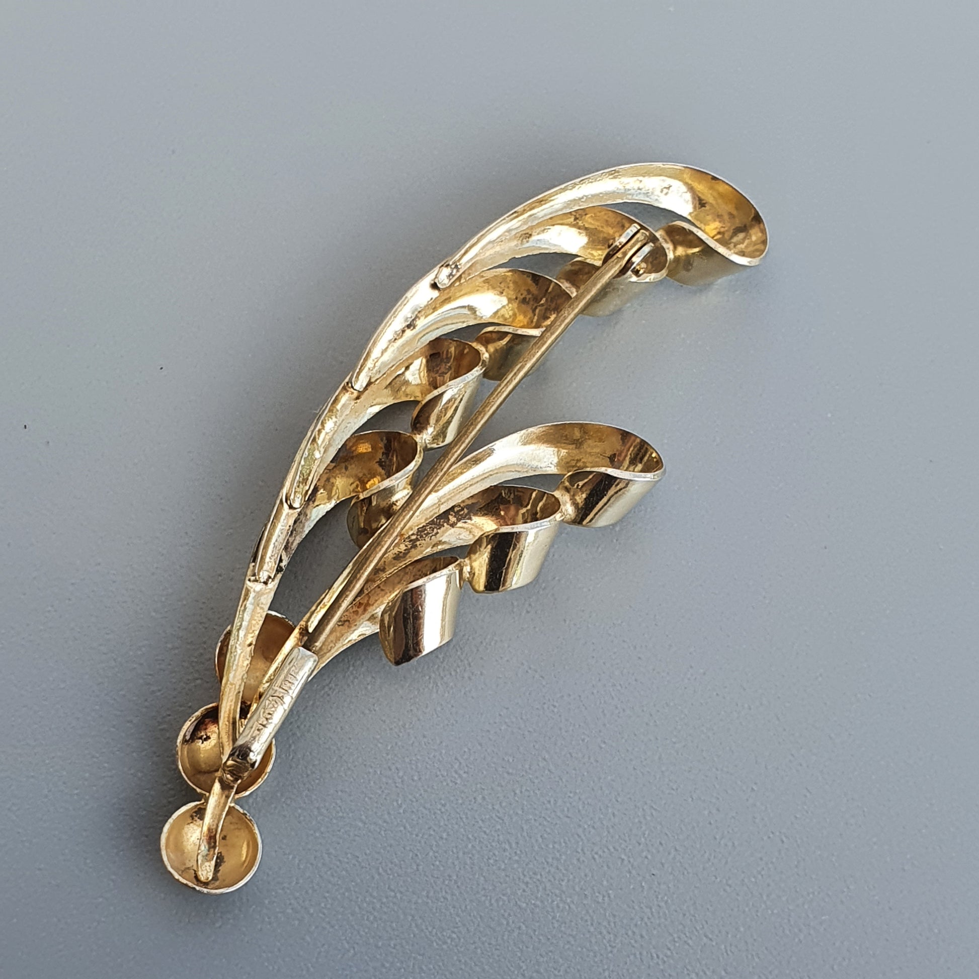 Gold-toned leaf-shaped brooch with curved, openwork design.