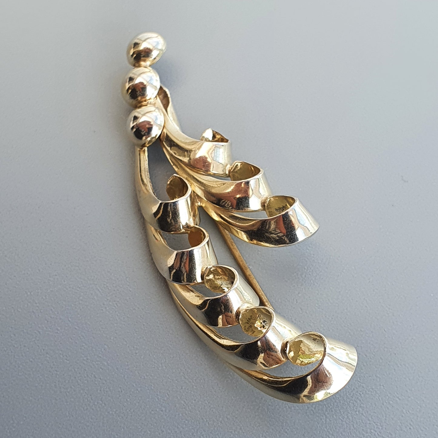 Gold-toned abstract brooch or pendant with curved, leaf-like shapes arranged in a cascading design.