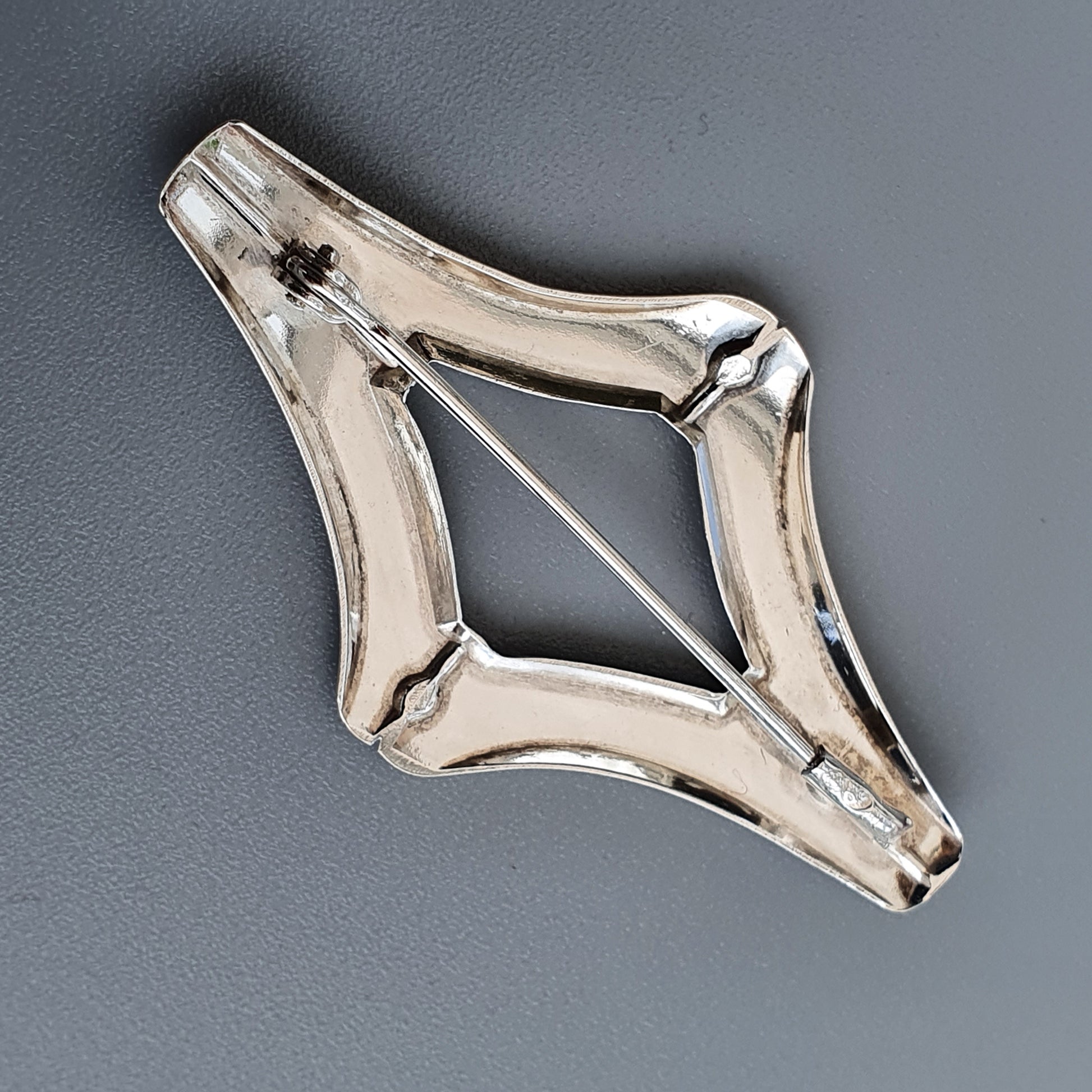 Diamond-shaped silver brooch or pendant with a hollow center and thin wire crosspiece.