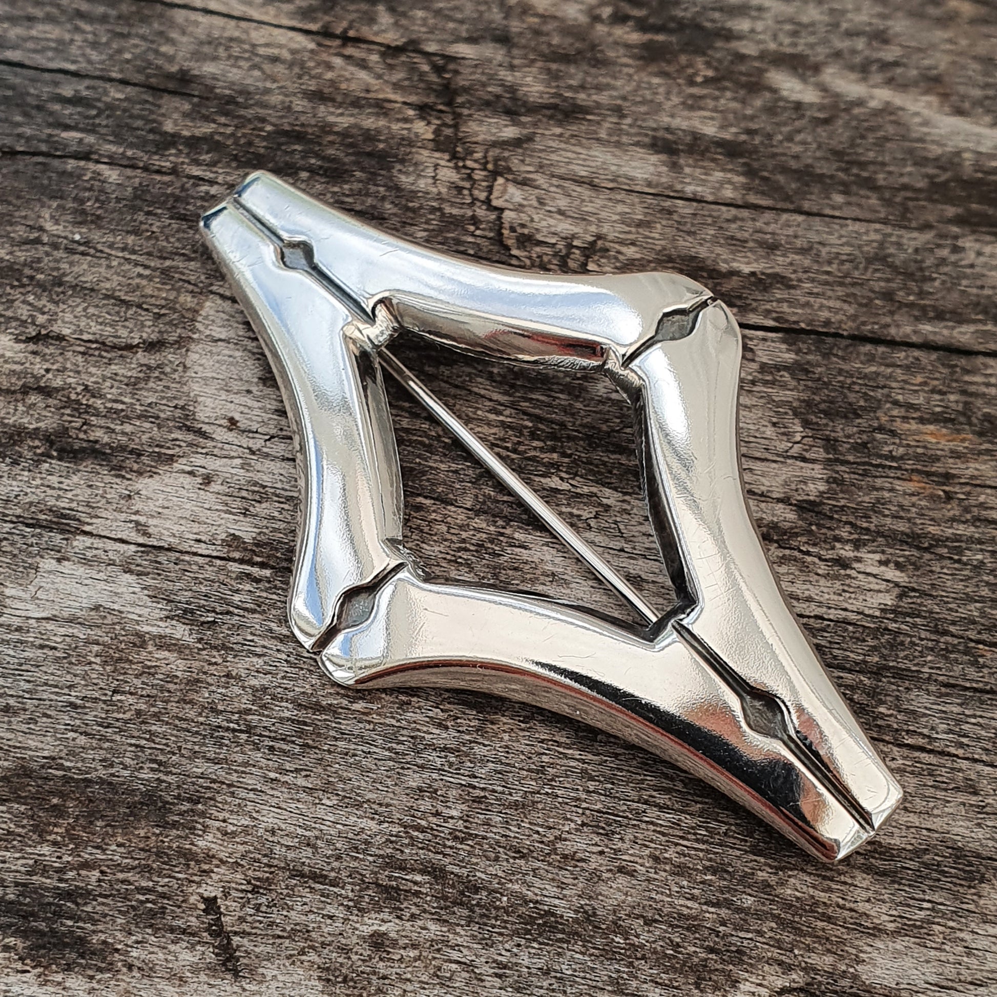 Silver-colored metal brooch or pendant with a diamond-shaped design and pointed edges.