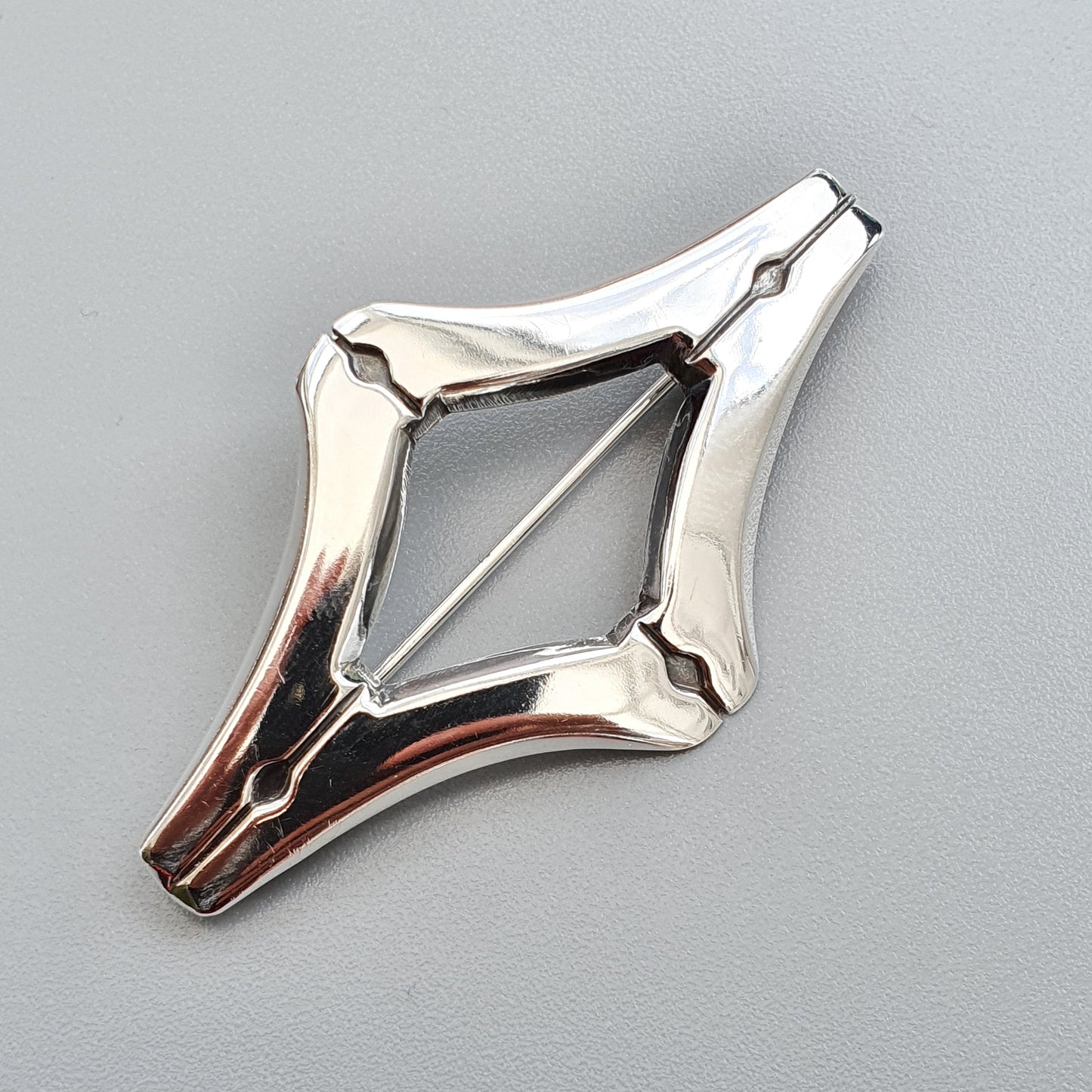 Silver-colored diamond-shaped brooch or pin with an open center.