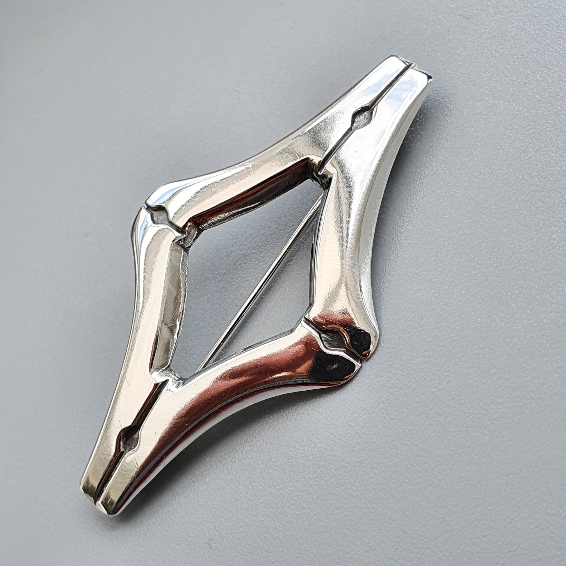 Metallic spring-loaded clamp or clip with a diamond-shaped opening.