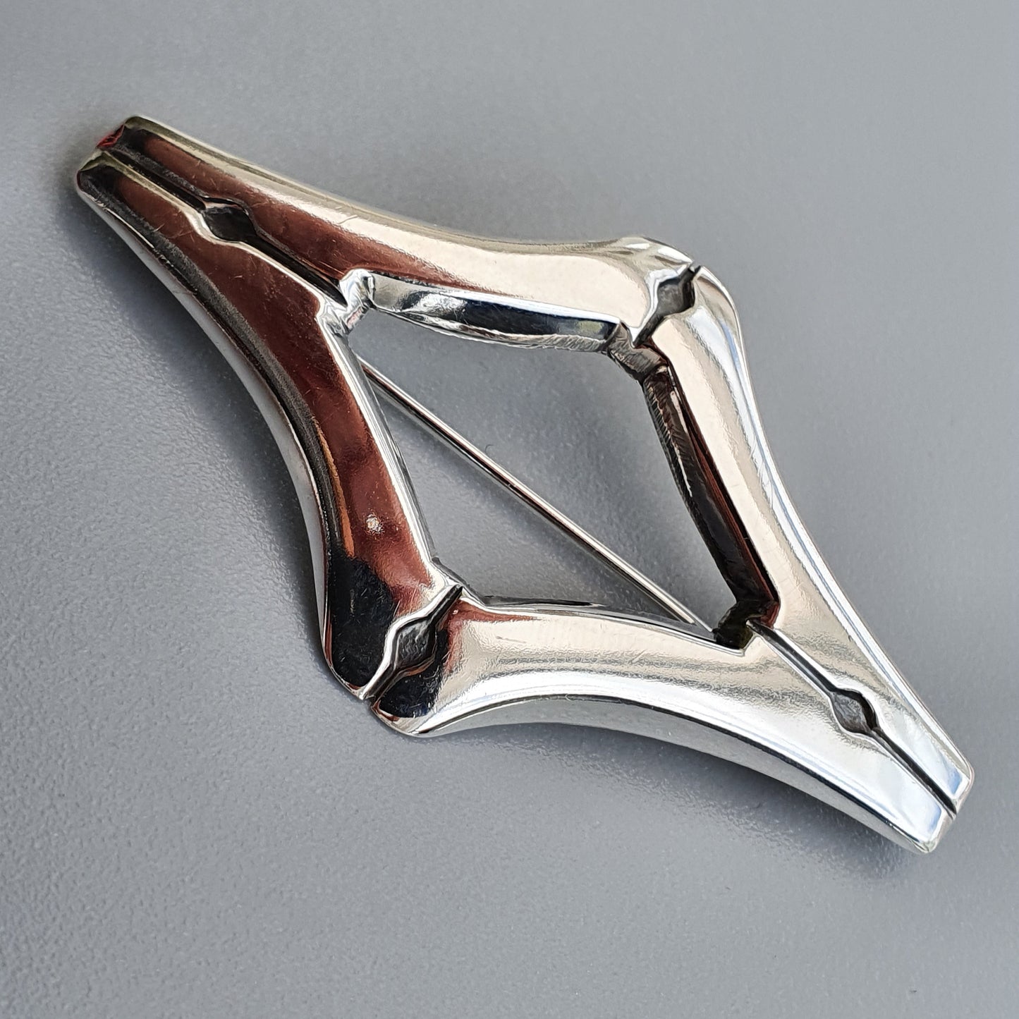 Diamond-shaped metal bottle opener with sleek, curved edges and a central opening.