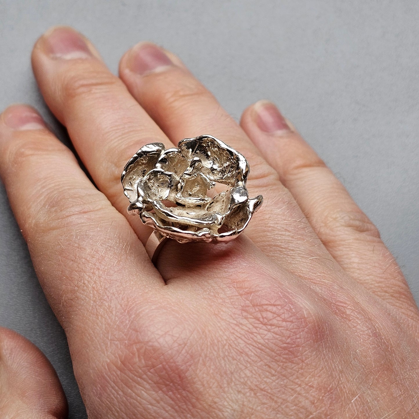 Ornate silver ring shaped like a blooming flower worn on a finger.