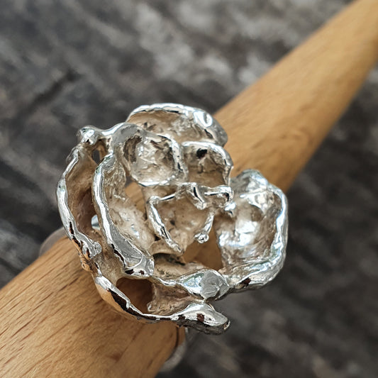 Silver rose-shaped ring on a wooden surface.