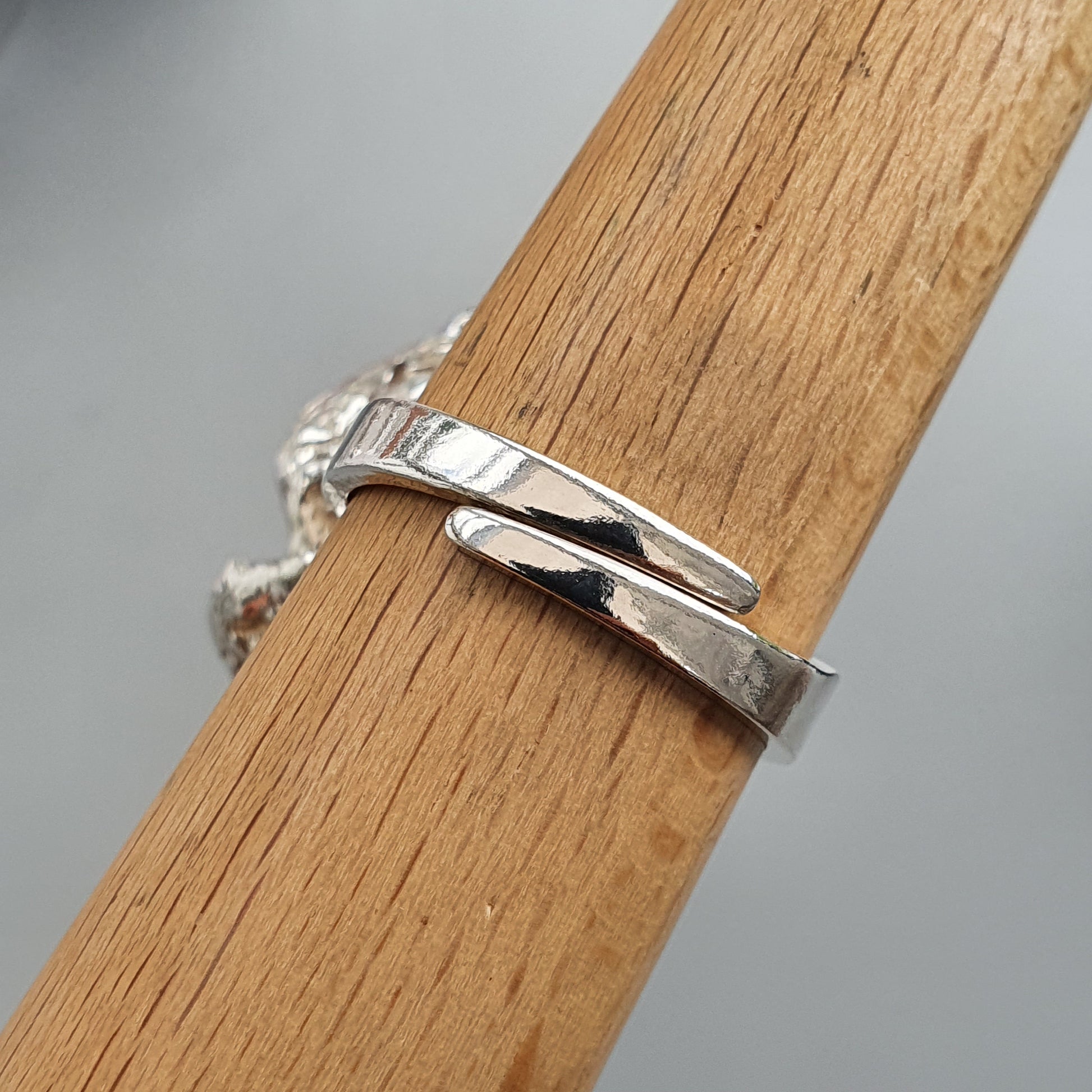 Silver ring with a unique overlapping design displayed on a wooden surface.