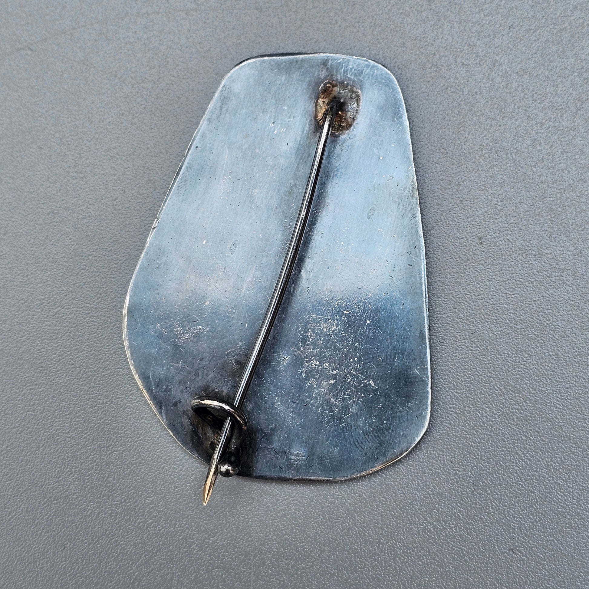 Irregularly shaped metallic brooch or pin with a long needle fastener.