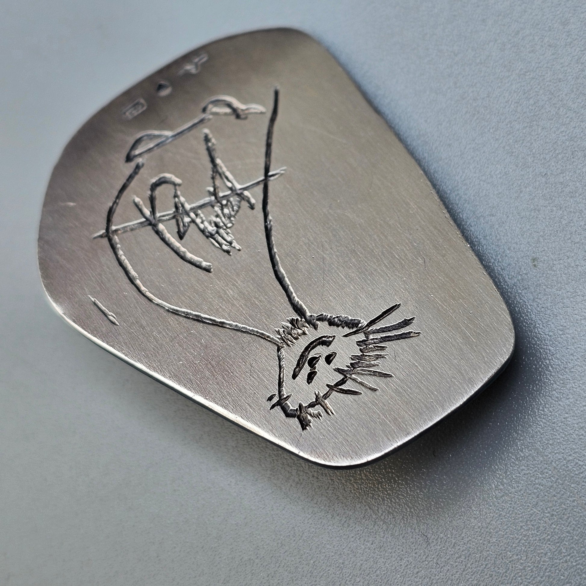 Metal guitar pick with an engraved cat design.