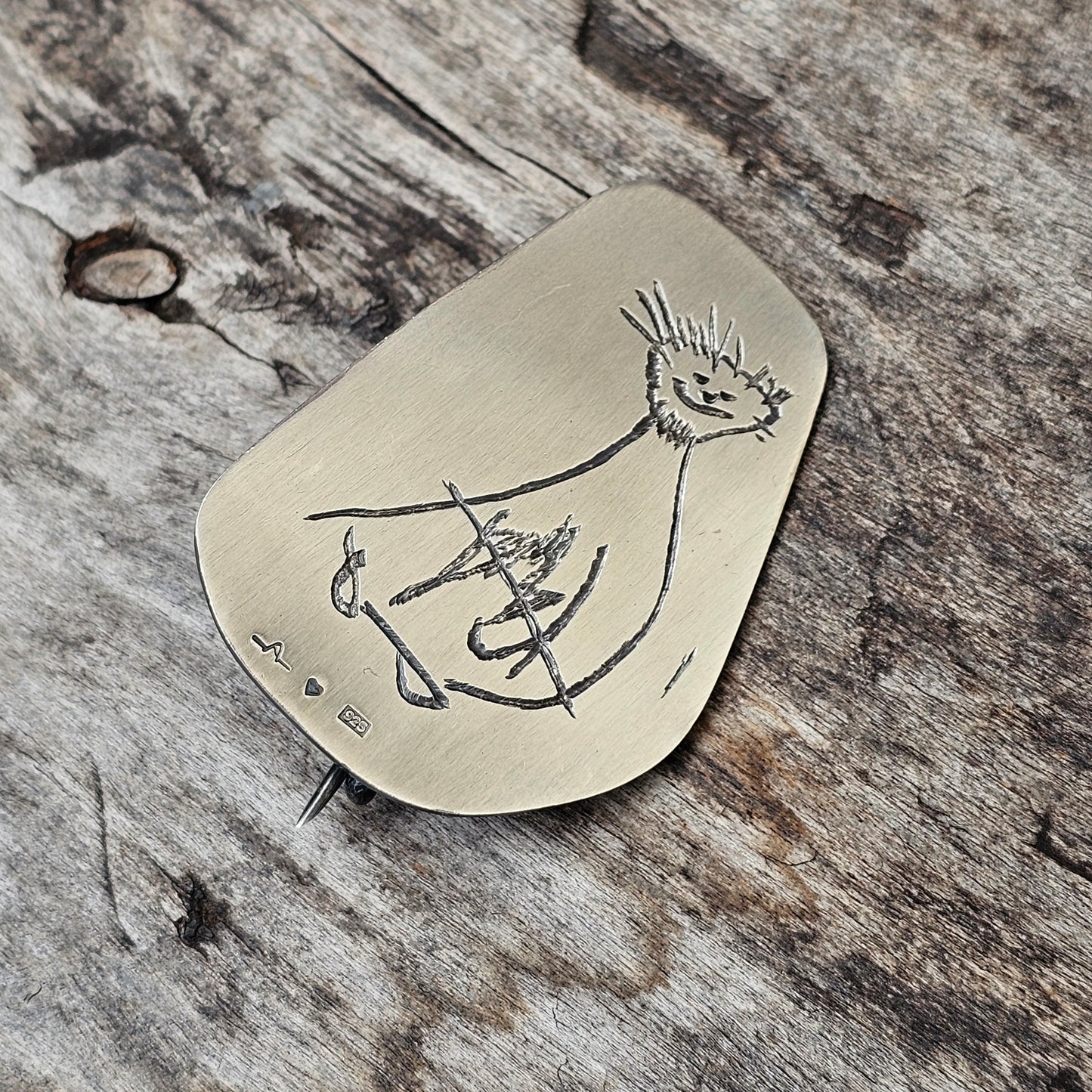 Metal pendant with an engraved abstract figure design.