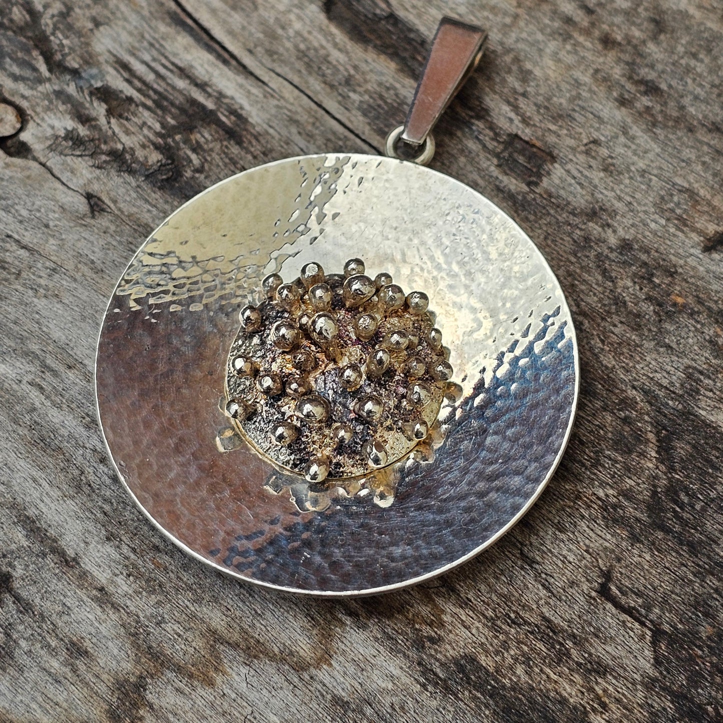 Circular silver pendant with a cluster of small gemstones in the center.