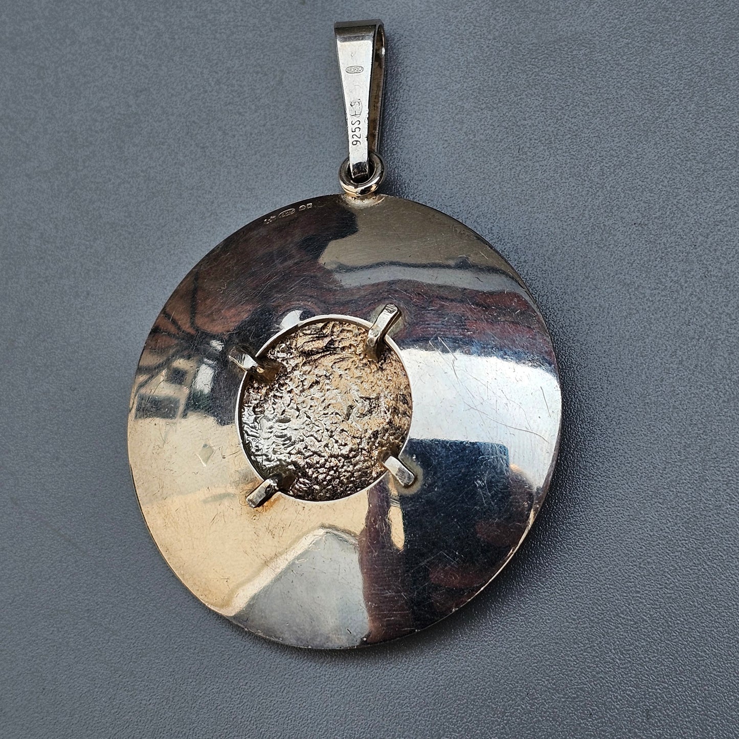 Circular silver pendant with a rough-textured stone or meteorite set in the center.