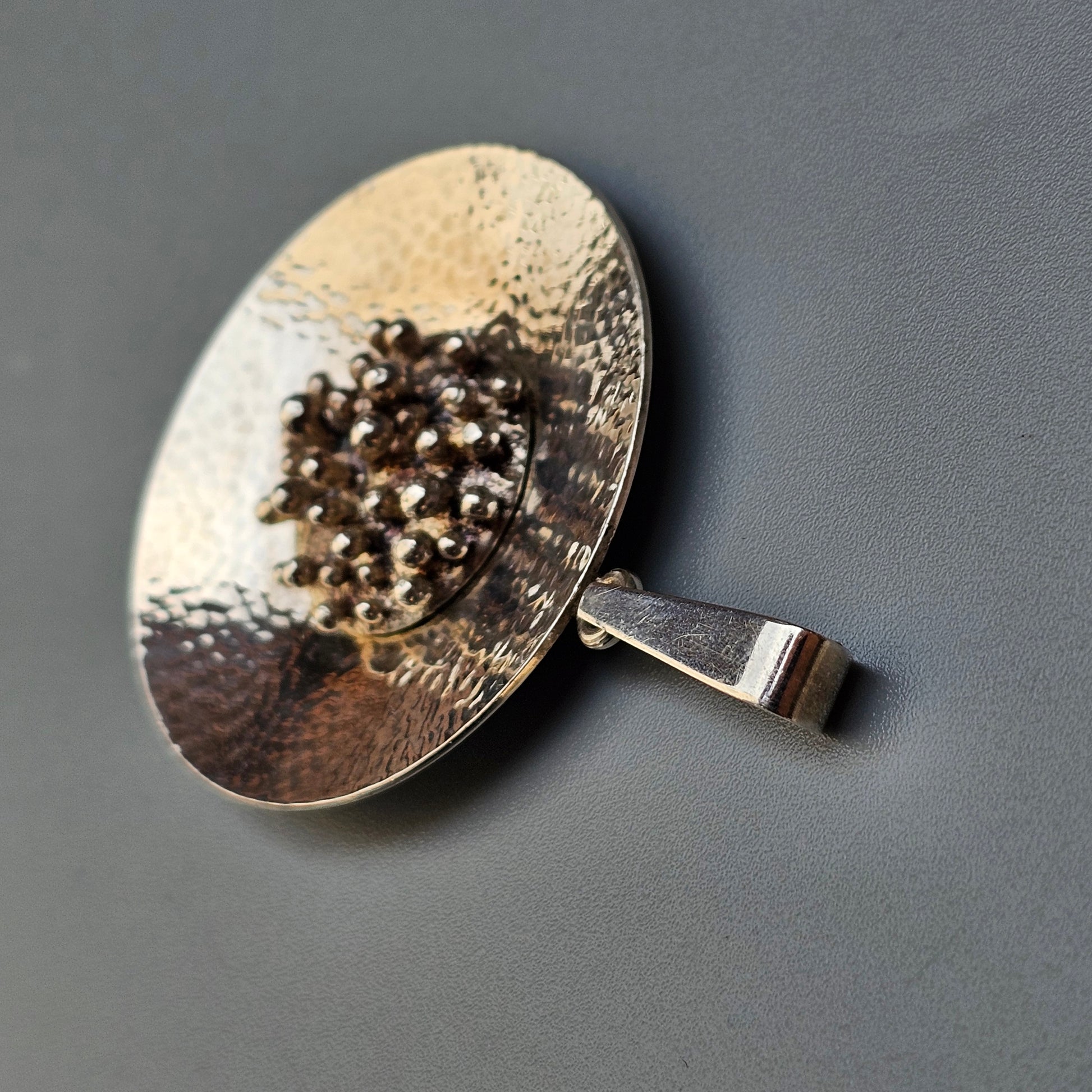 Hammered metal spoon or ladle containing black peppercorns.