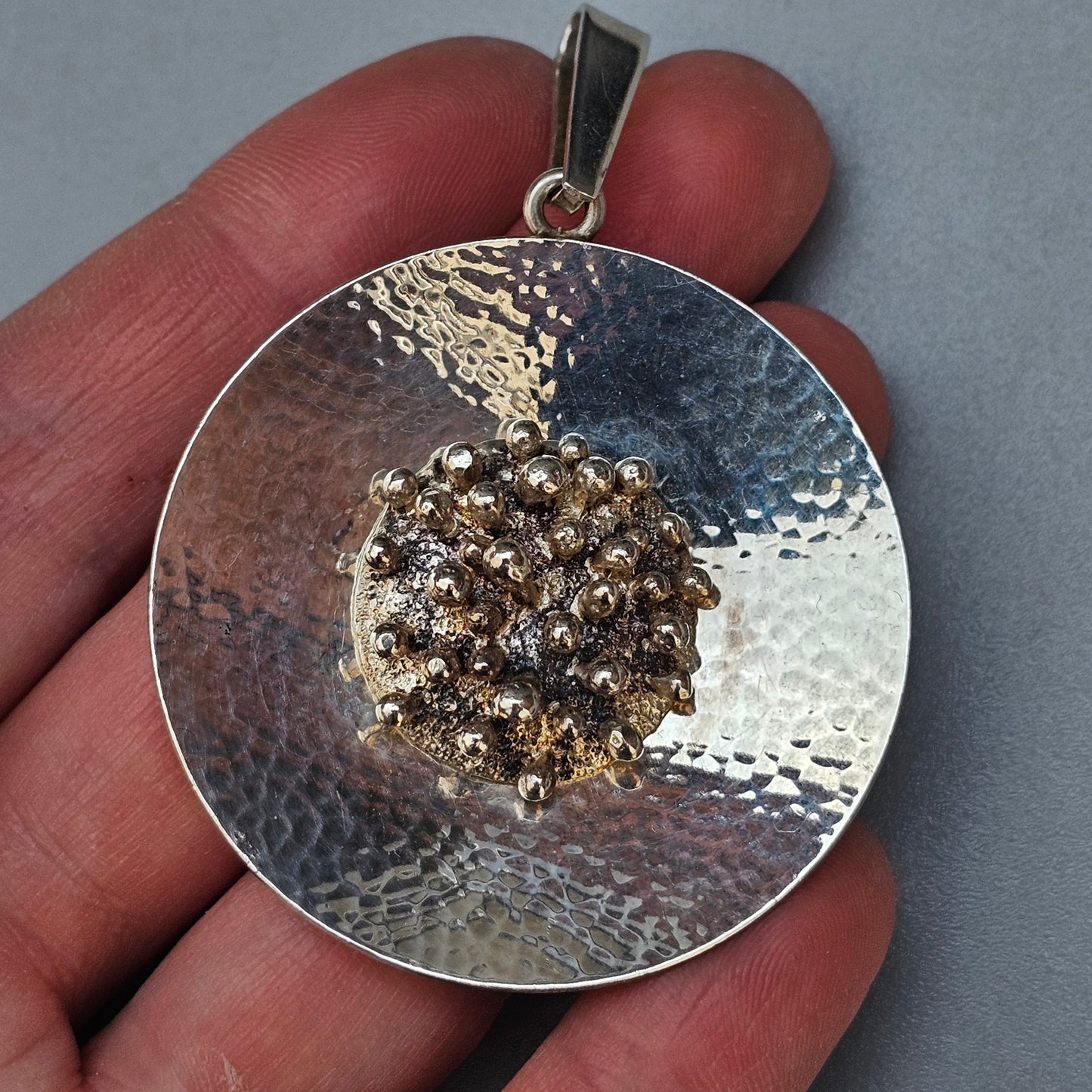 Circular silver pendant with a textured surface and a cluster of golden crystals or stones in the center.