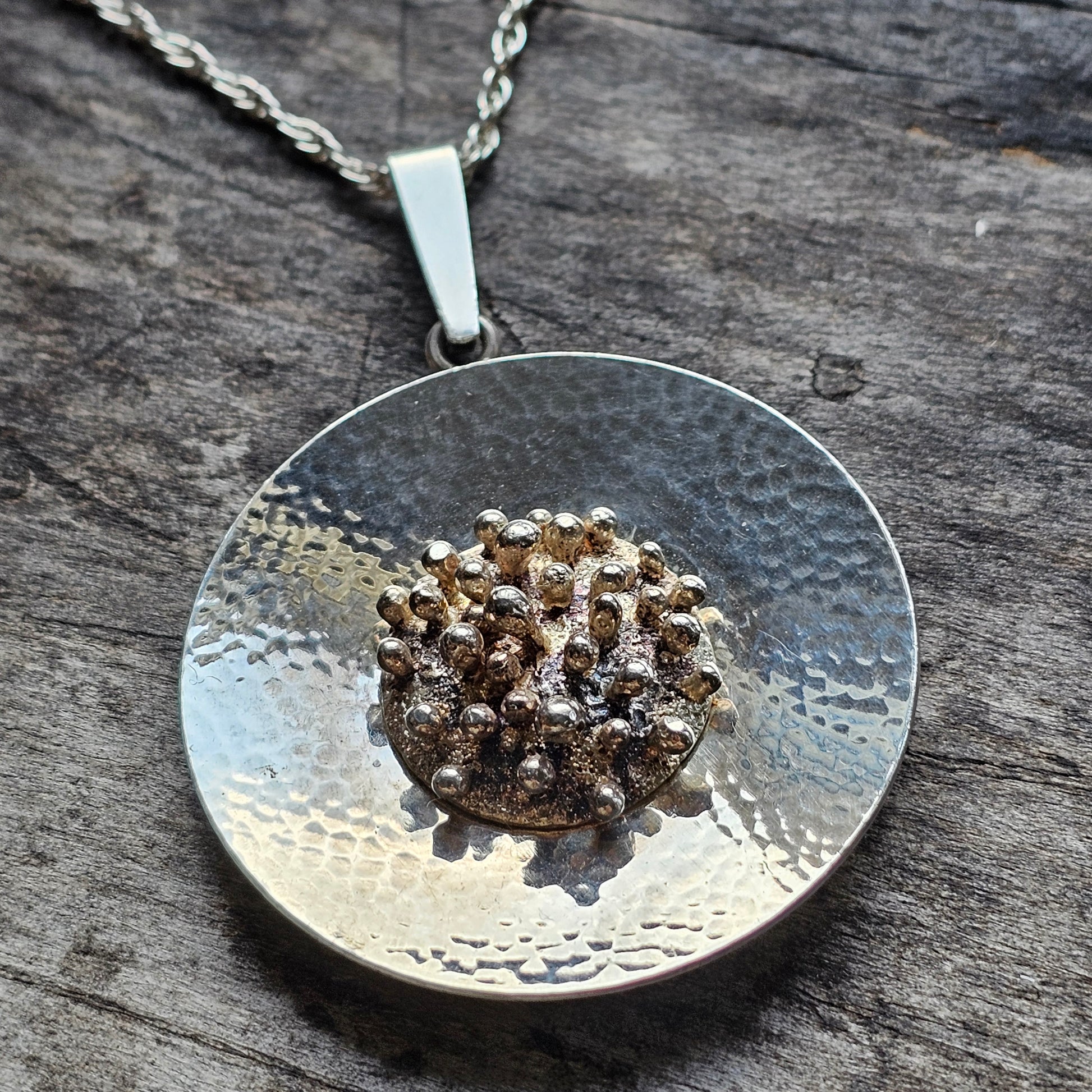 Silver pendant necklace featuring a textured circular disc with a golden, bumpy center.