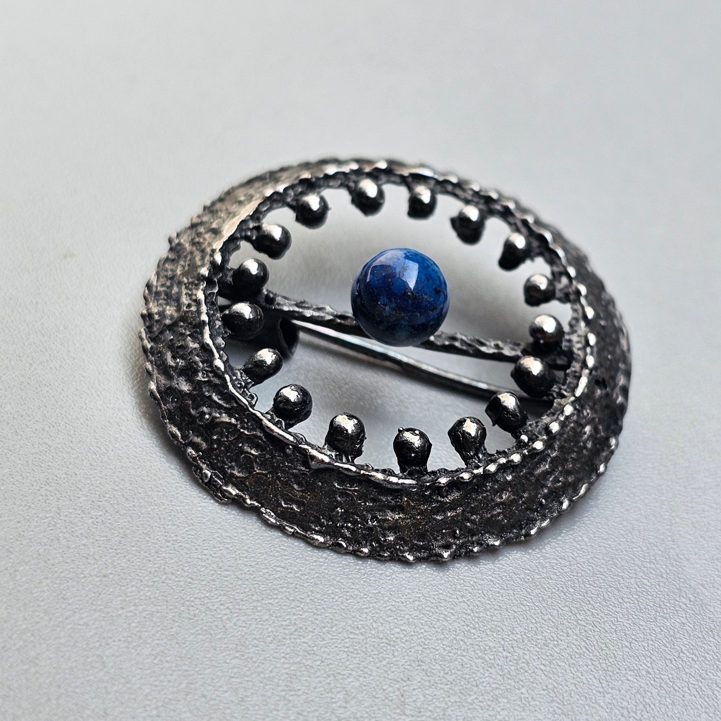 Ornate silver brooch or pendant featuring a blue gemstone at its center.