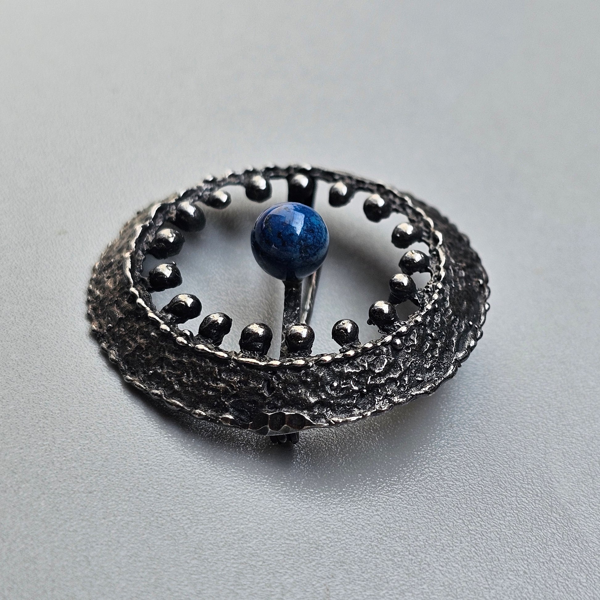 Ornate silver brooch or pendant with a central blue stone or bead.