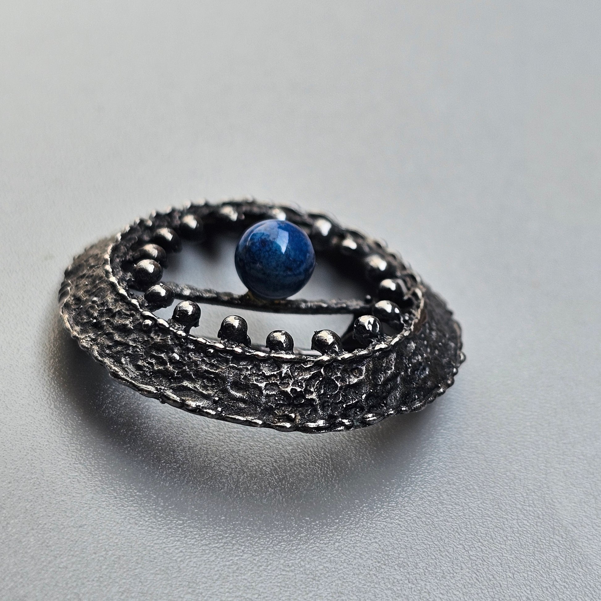 Intricate silver ring with a blue gemstone set in an ornate, textured band.