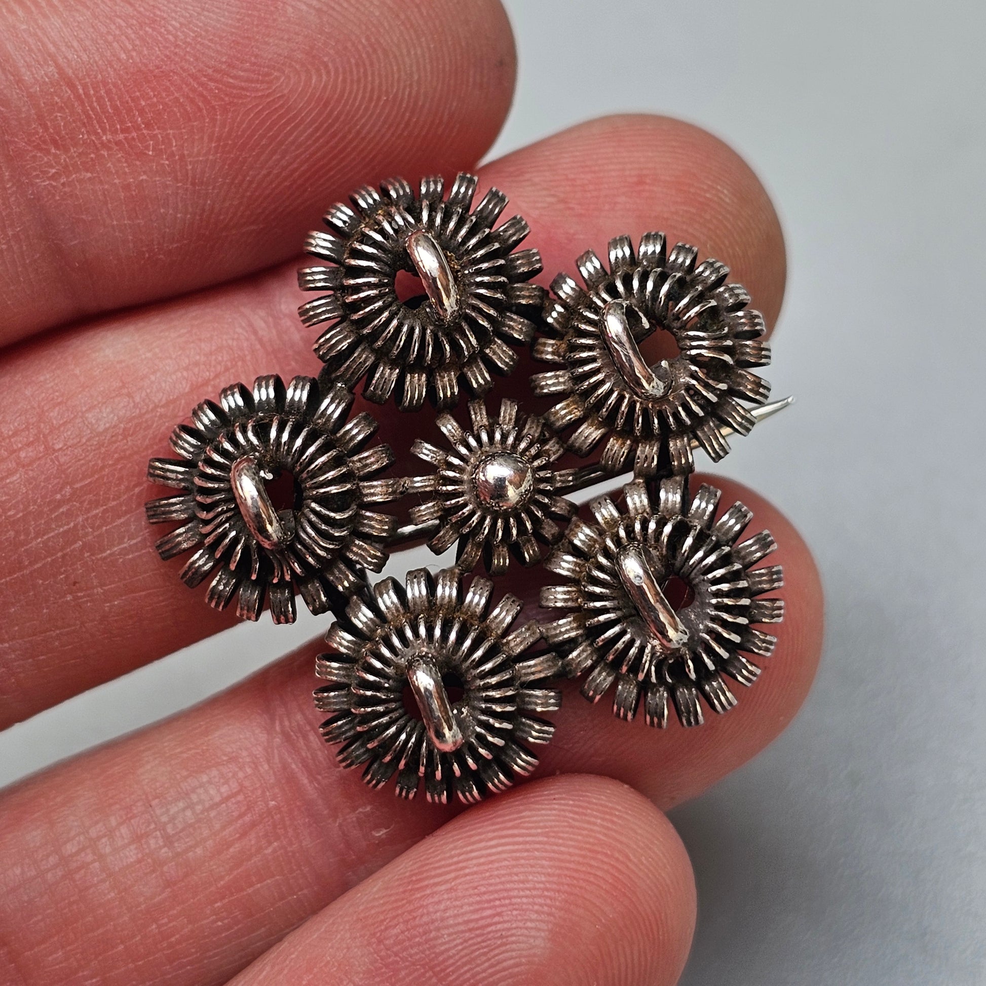 Intricate silver brooch with five circular floral-like designs clustered together.