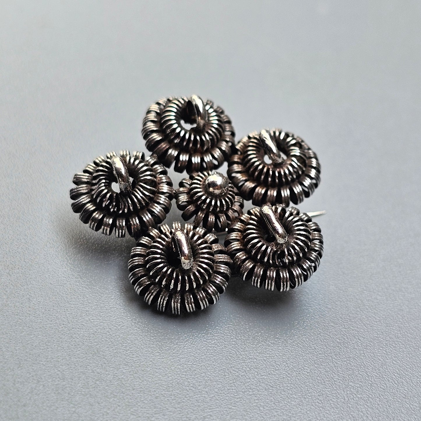 Cluster of five spiral-shaped metallic beads or charms with intricate coiled designs.