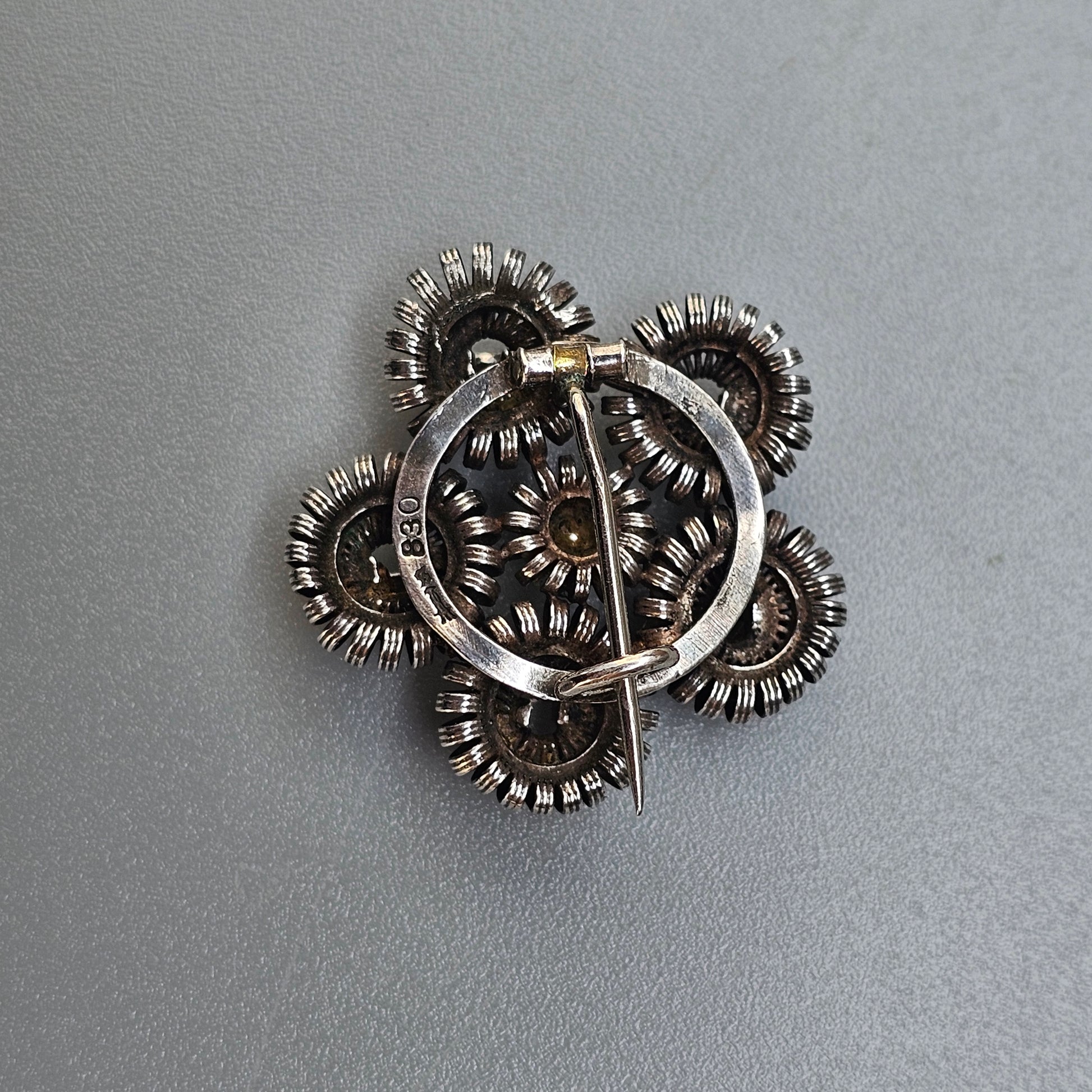 Intricate silver brooch or pin shaped like a stylized flower with multiple layered petals.