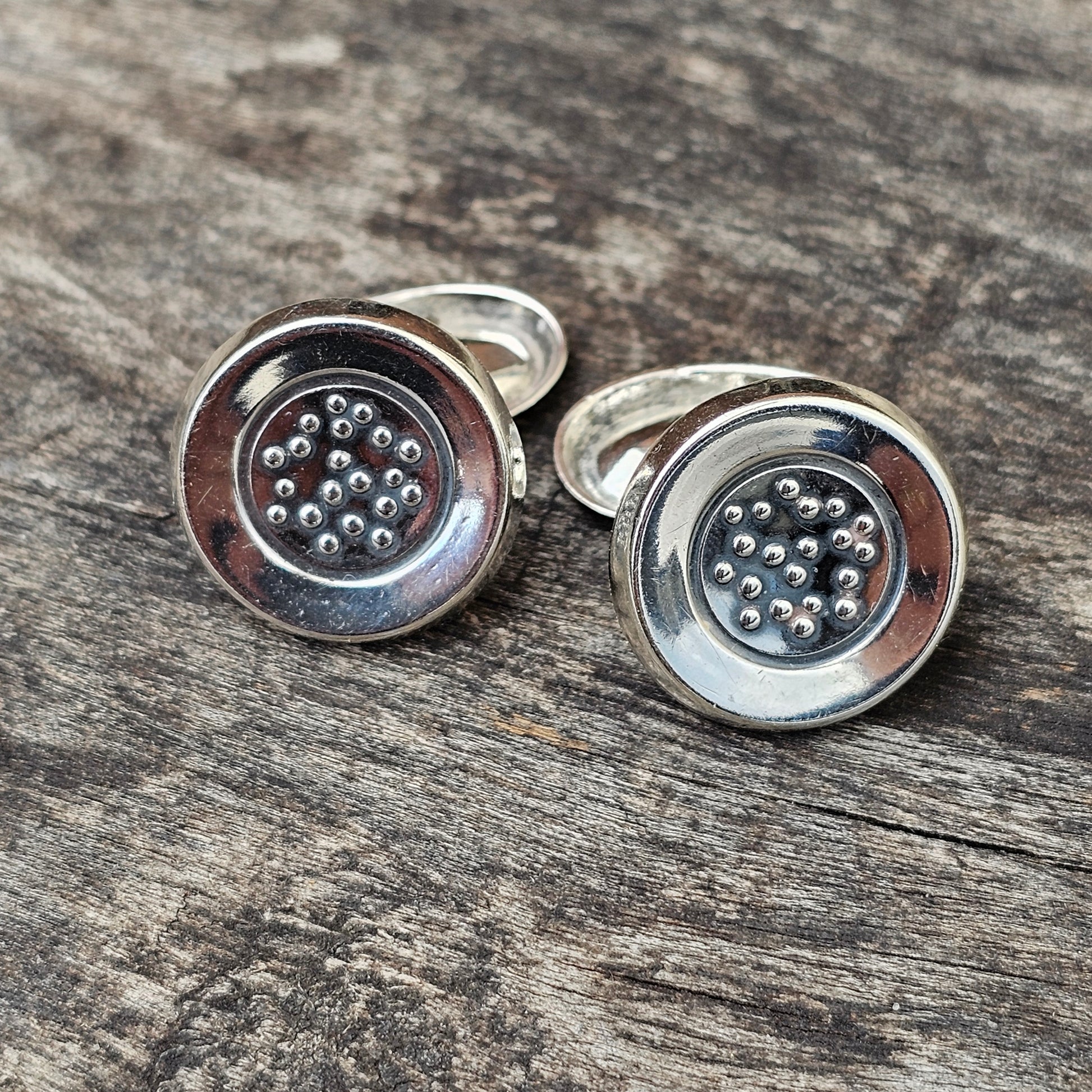 Pair of silver cufflinks with circular designs featuring small metallic beads.