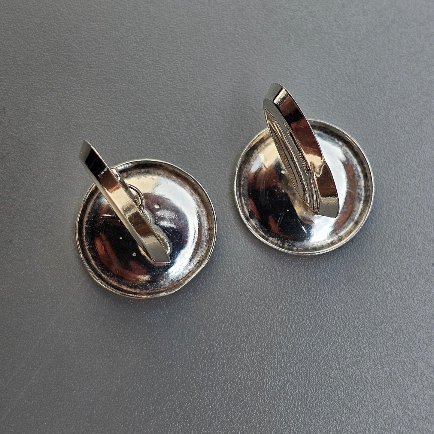 Pair of silver-colored clip-on earrings with circular bases and curved attachments.