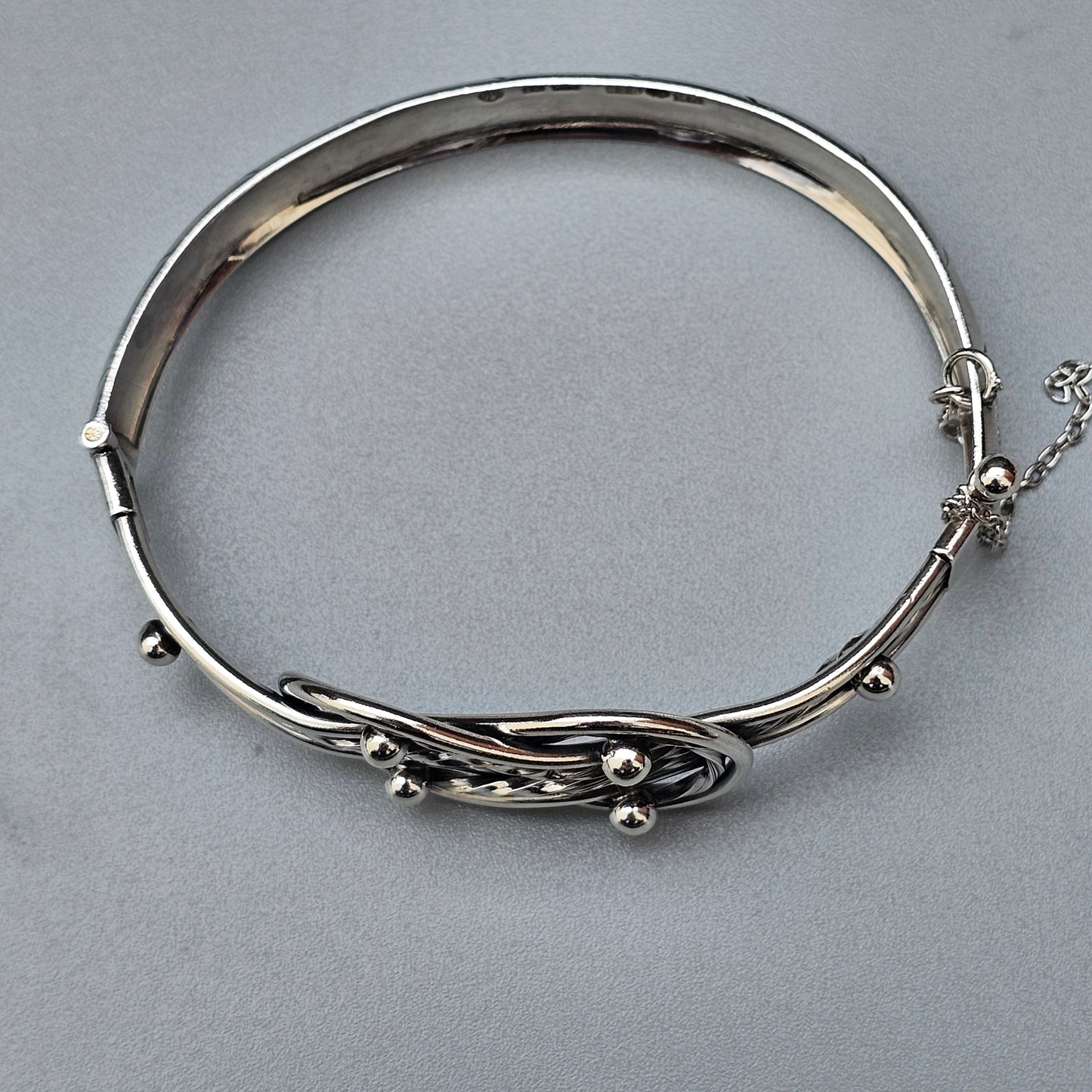 Silver bangle bracelet with an intricate twisted wire design and small bead accents.