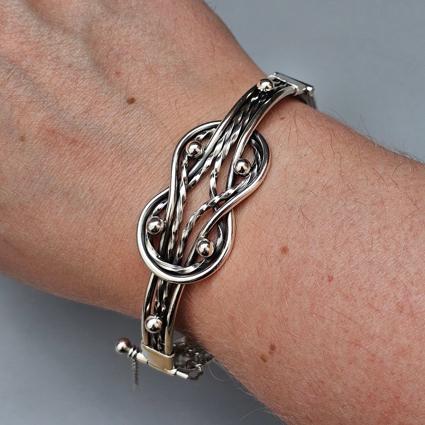 Silver bracelet with an intricate knot design and small beads.