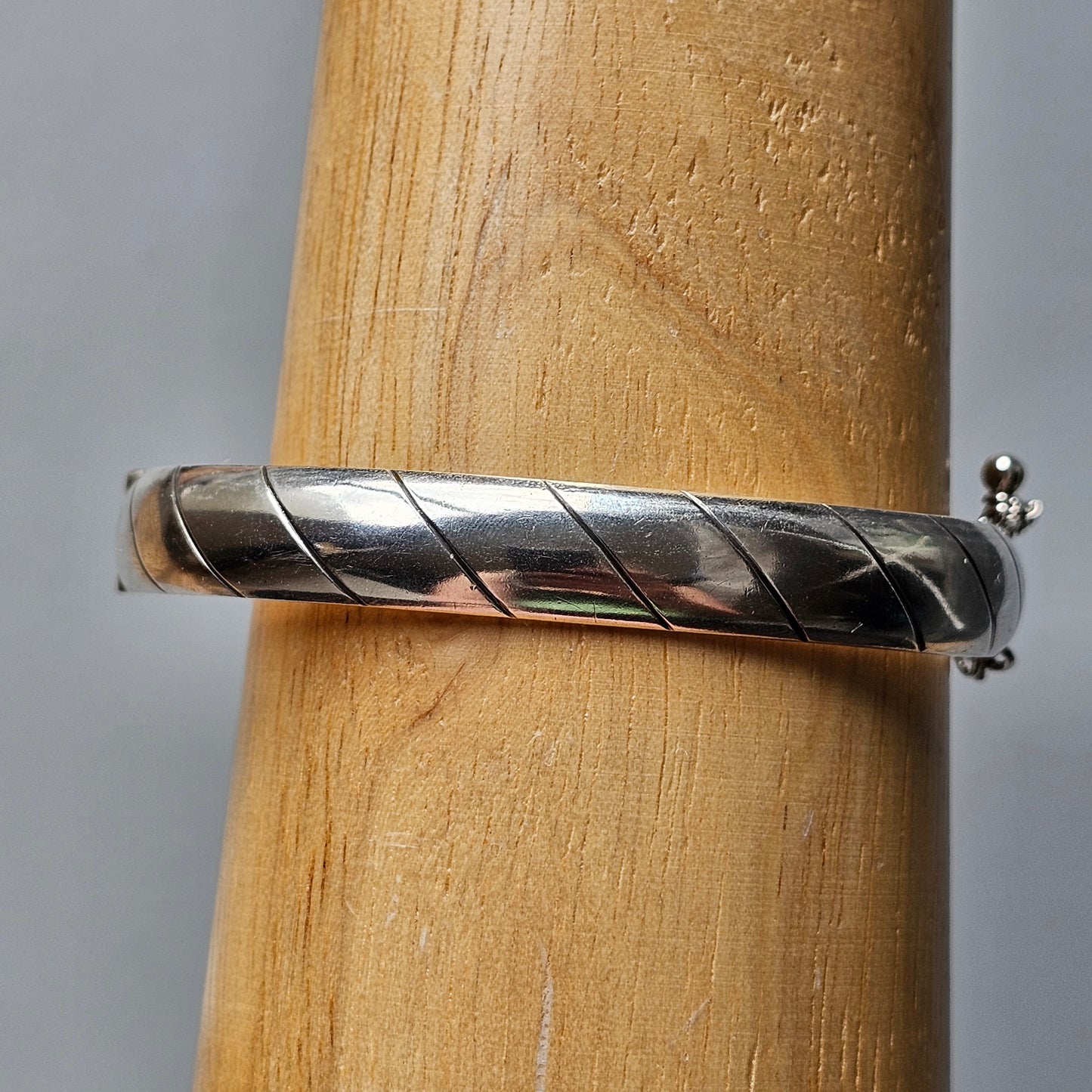 Silver bangle bracelet with a spiral pattern wrapped around a wooden cylinder.