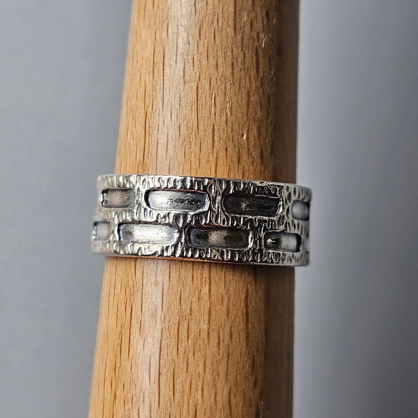 Silver ring with a textured brick-like pattern around its band.