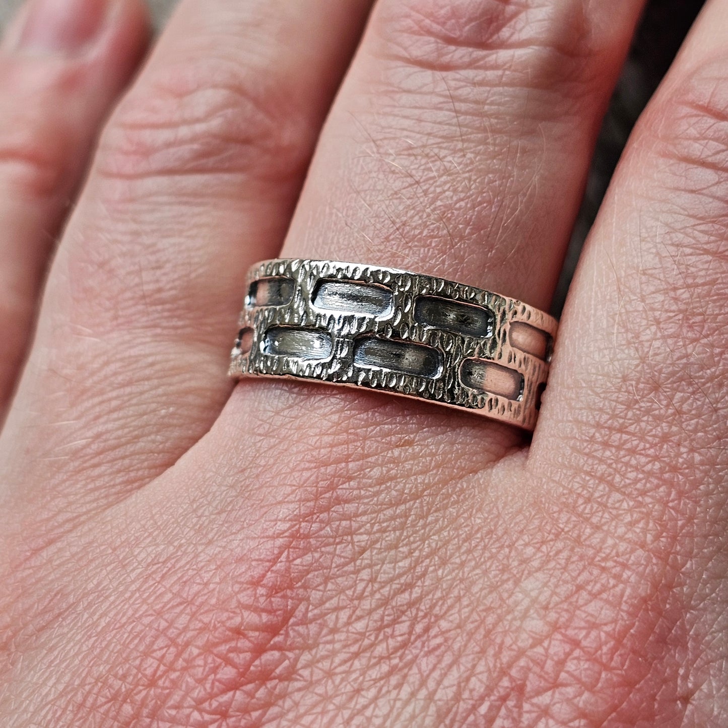 Silver ring with a textured, geometric pattern worn on a finger.